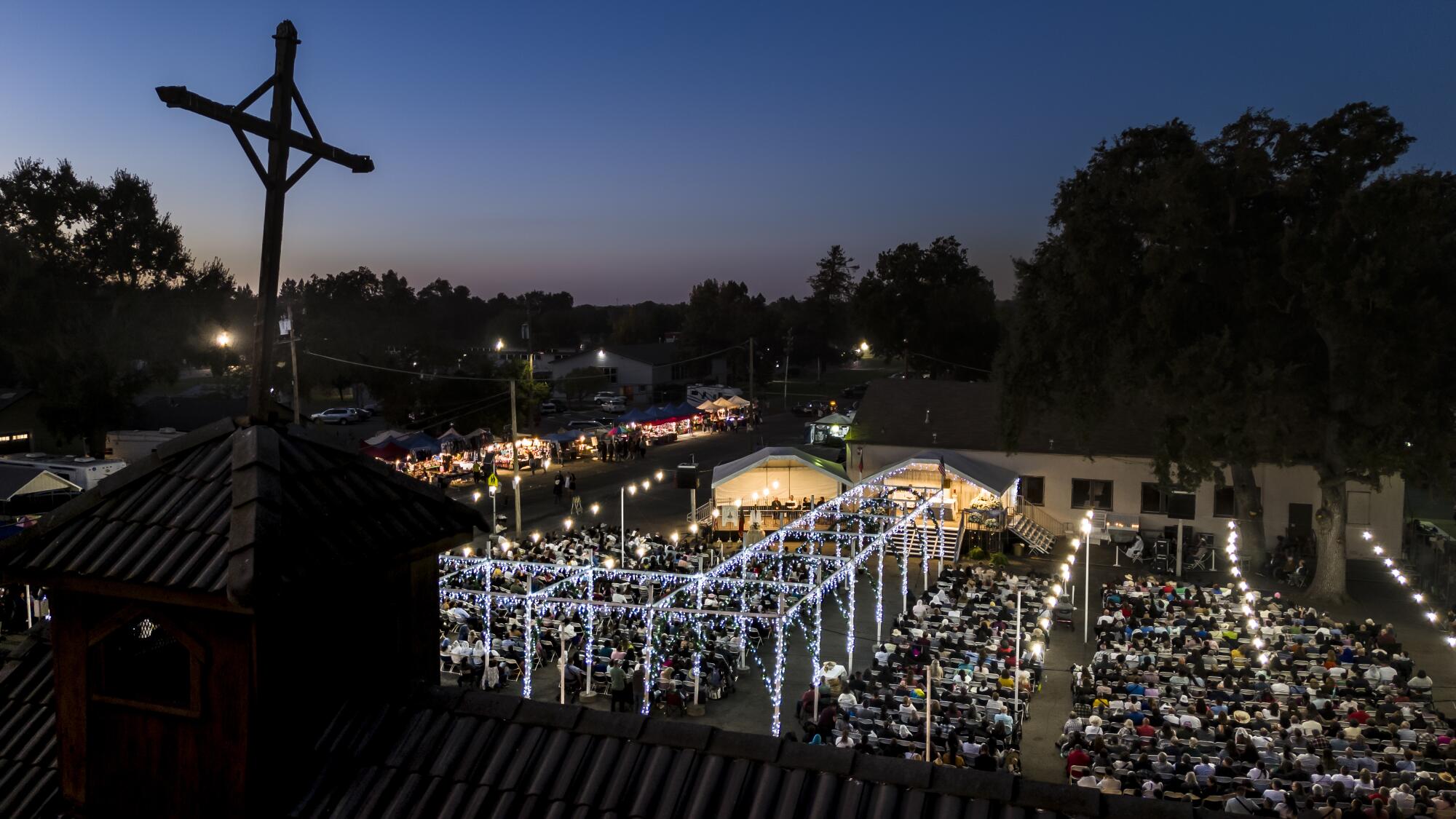 A rooftop cross looms over crowds of people below