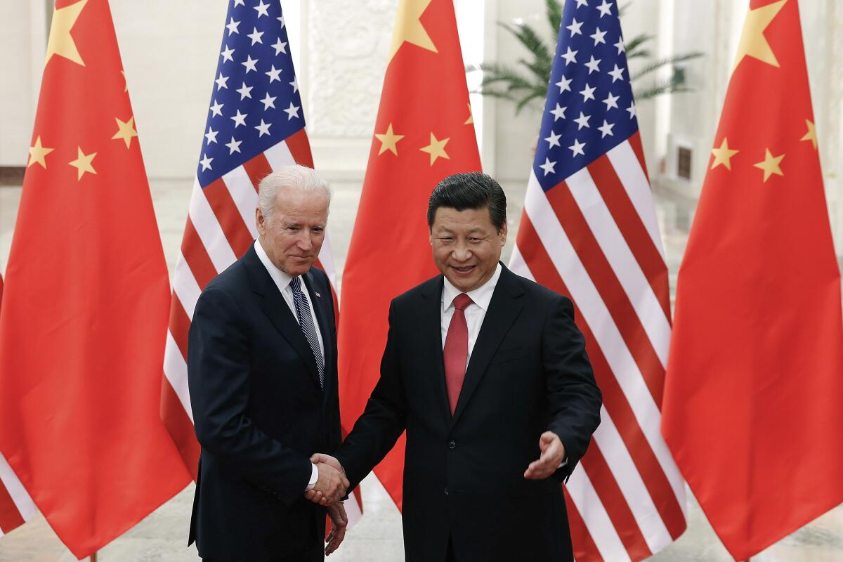 A man with gray hair, in dark suit and blue tie, left, shakes hands with a man with dark hair, in dark suit and red tie