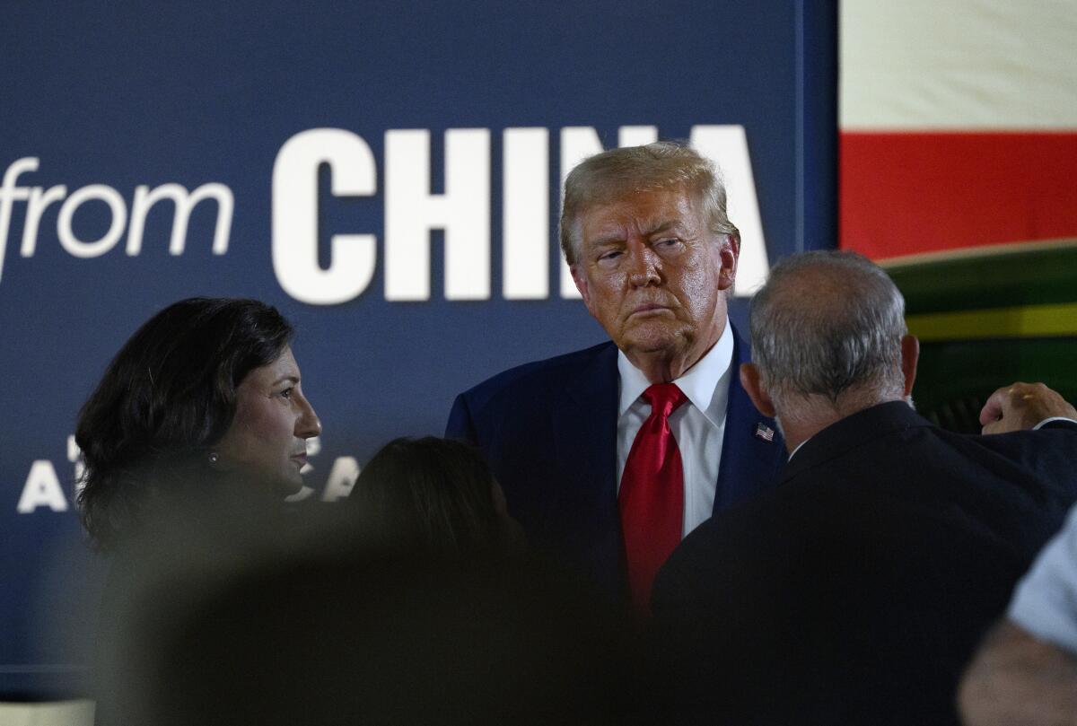 A man in a dark suit and red tie listens as other people stand near him