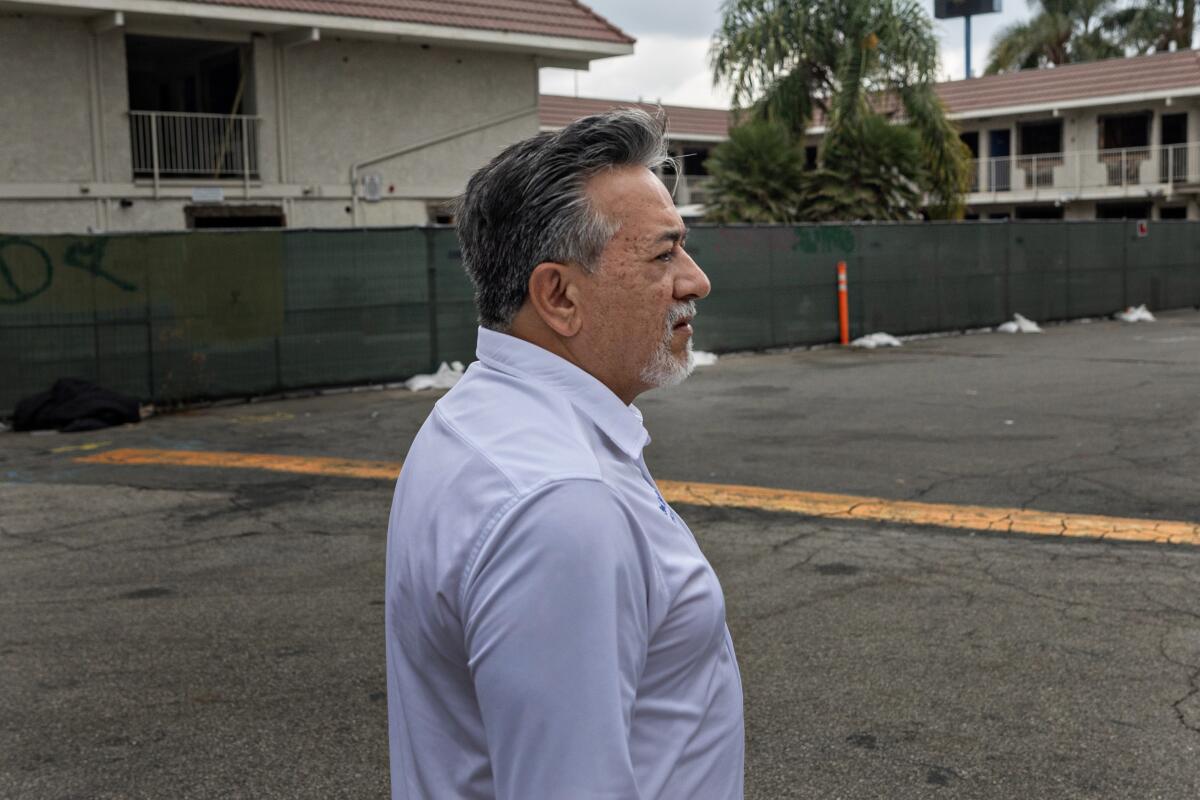 A man stands on a large asphalt area near a speedbump.