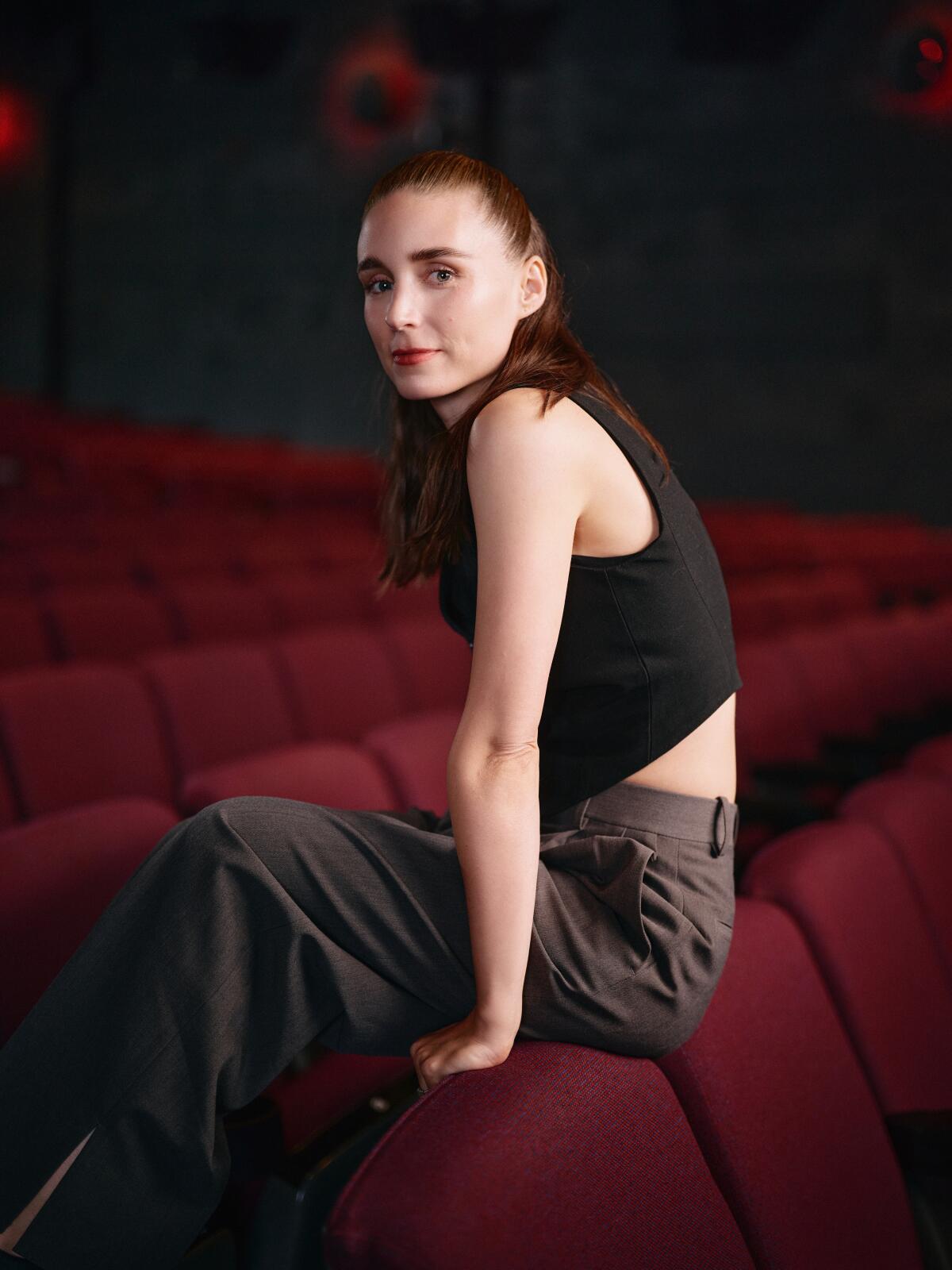 A woman in a black tank top sits on the back of a movie seat.