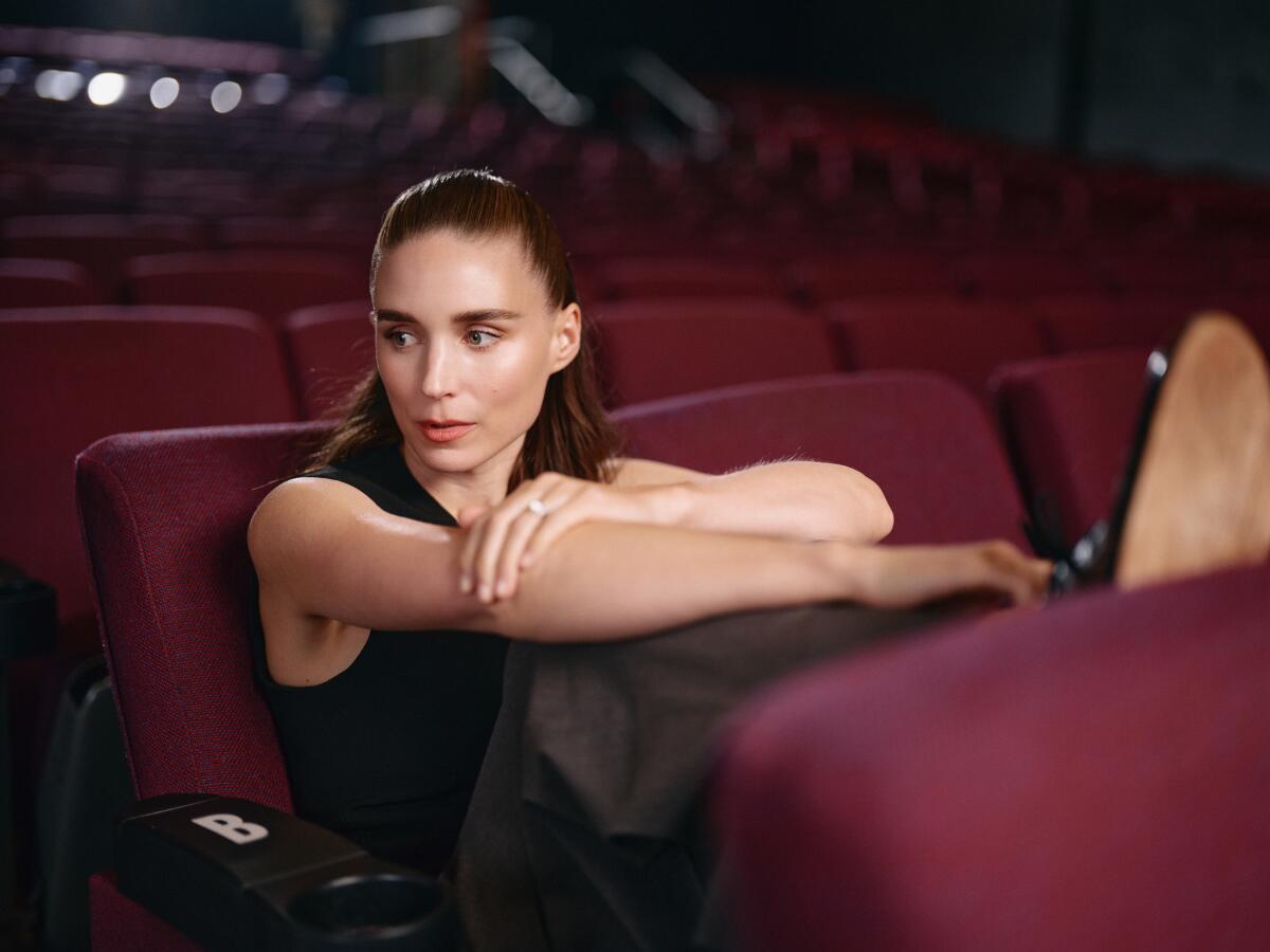 A woman in a black tank top sits in an empty movie theater, looking to the side.