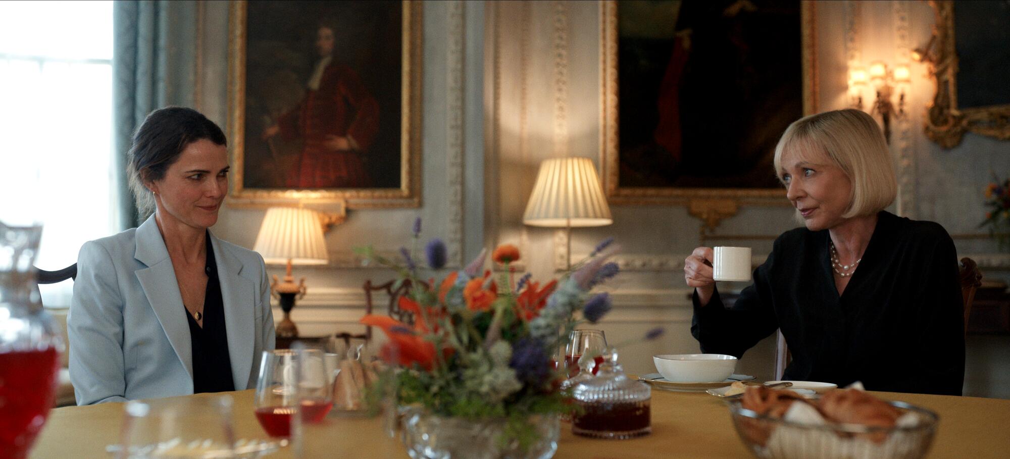 A woman wearing a baby blue suit sits next to a woman in a black suit.