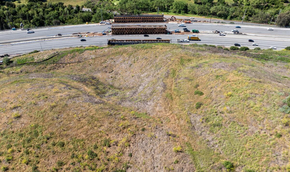 A highway sits at the bottom of a large grassy hill. Construction can be seen on the sides of the highway.