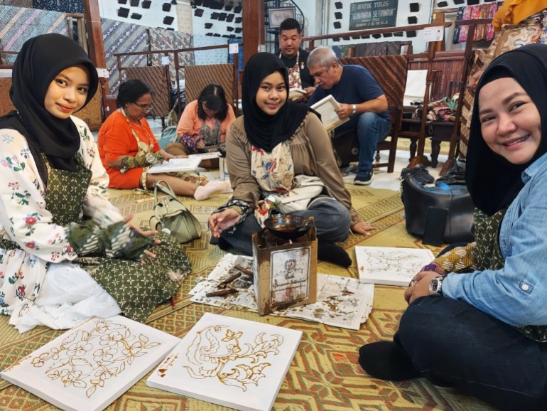 Young women at a batok class in Solo. They are sitting on the floor around a wax burner. There are square of framed white cloth on the floor.