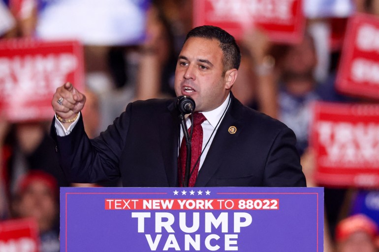 Anthony D'Esposito gestures and speaks into a microphone emblazoned with a Trump-Vance sign.