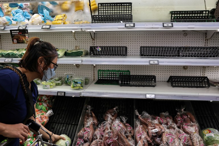 Empty shelves in a Taiwan supermarket. A woman is picking out some of the few remaining vegetables