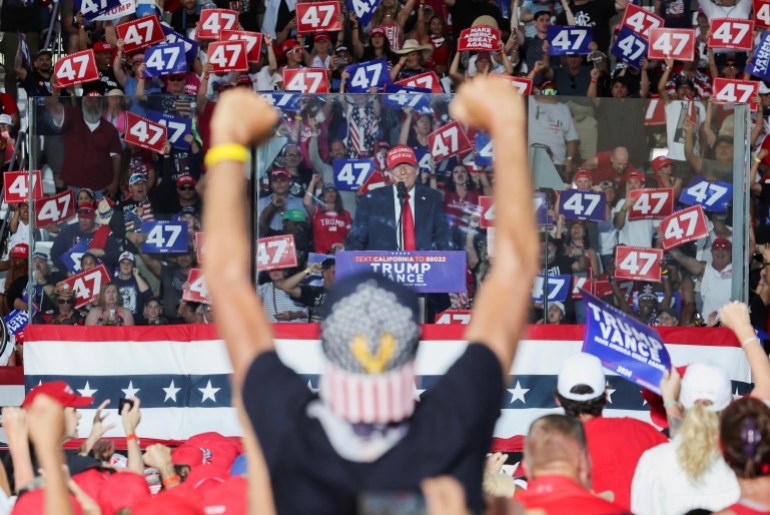 A Trump supporter holds up both hands in fists as the former president speaks in front of him at a rally.