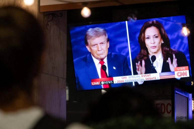 A walking past stops to watch a screen displaying the US Presidential debate between Vice President and Democratic presidential candidate Kamala Harris and former US President and Republican presidential candidate Donald Trump