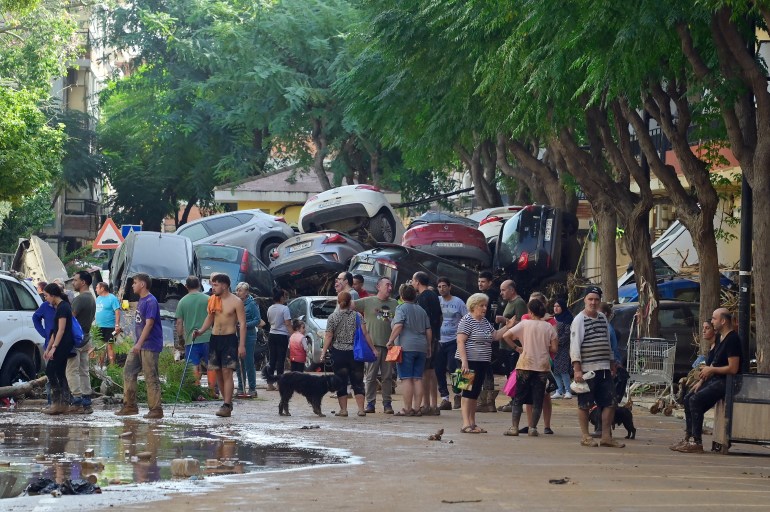 Residents gather in the street next to a pile of cars on October 31, 2024 after flash floods affected the town of Massanassa, in the region of Valencia, eastern Spain. - Rescuers raced on October 31, 2024 to find survivors and victims of once-in-a-generation floods in Spain that killed at least 95 people and left towns submerged in a muddy deluge with overturned cars scattered in the streets. About 1,000 troops joined police and firefighters in the grim search for bodies in the Valencia region as Spain started three days of mourning. Up to a year's rain fell in a few hours on the eastern city of Valencia and surrounding region on October 29 sending torrents of water and mud through towns and cities. (Photo by JOSE JORDAN / AFP)