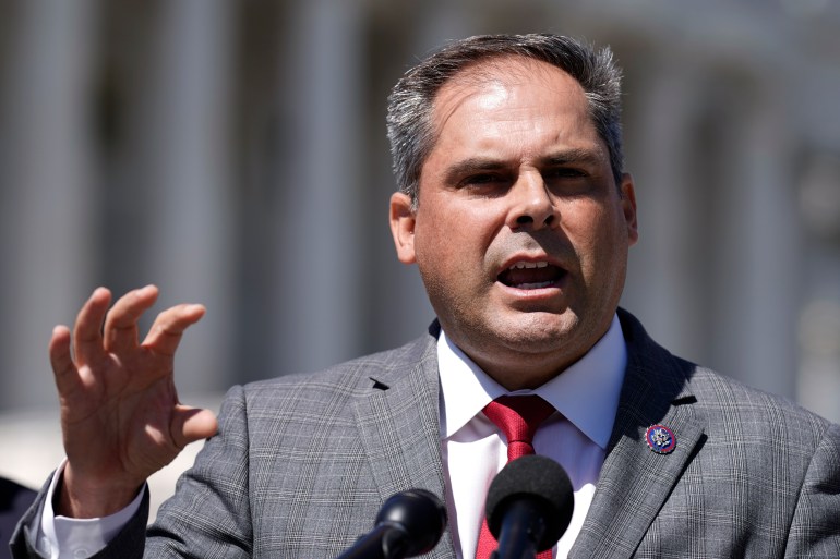 Mike Garcia stands outside and gestures behind a podium as he speaks.