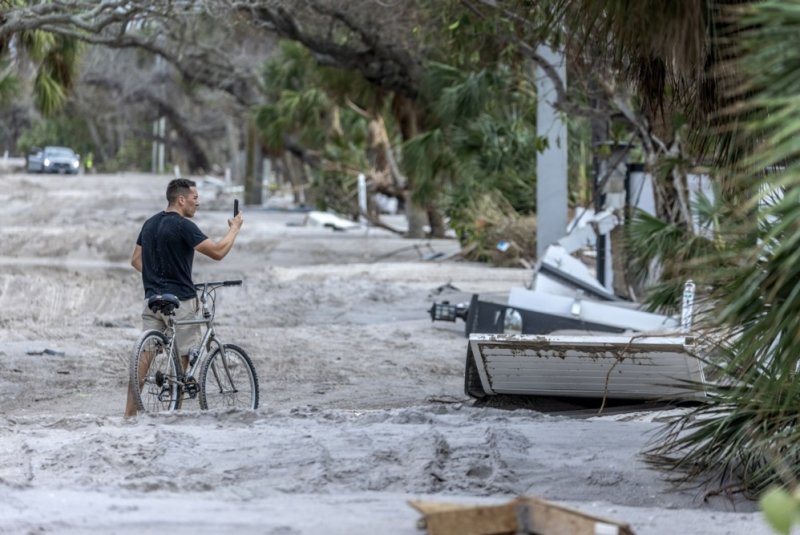 A person takes a photo of a property from a road covered in sand after Hurricane Milton's landfall in Manasota Key, Fla., on Friday. President Joe Biden on Saturday approved a federal disaster aid package for 34 hard-hit counties in Florida. Photo by Cristobal Herrera-Ulashkevich/EPA-EFE