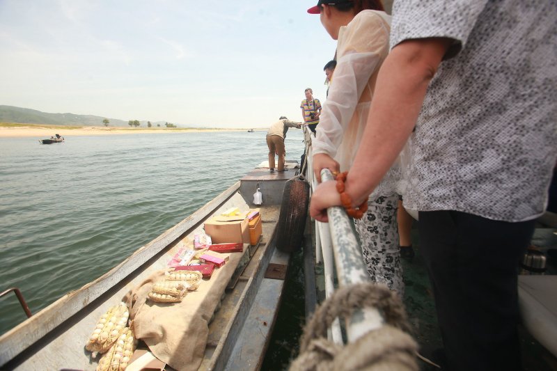 A North Korean man sells contraband pickled eggs, cigarettes, alcohol and ginseng to Korean, Japanese and Chinese tourists on the Yalu River, north of Dandong, China's larger border city with North Korea (background), in Liaoning Province, on May 29, 2015. Counterfeit cigarettes are an important revenue source for North Korea, and a Chinese national was extradited to the United States this week to faces charges over aiding Pyongyang in producing the contraband. File Photo by Stephen Shaver/UPI