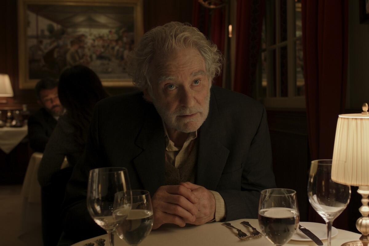 An older man in a suit jacket leaning over a dining table in a dimly lit room.