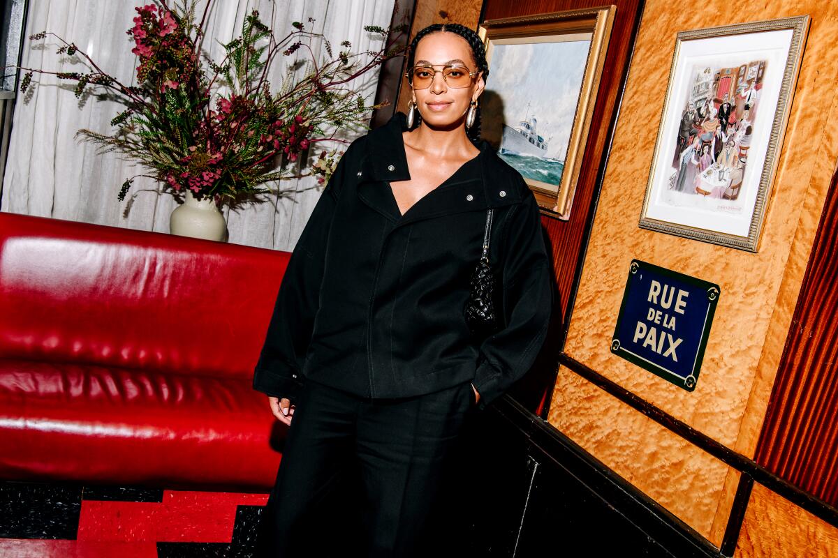 Solange Knowles stands next to a board that holds a painting and a sign that reads Rue de la Paix