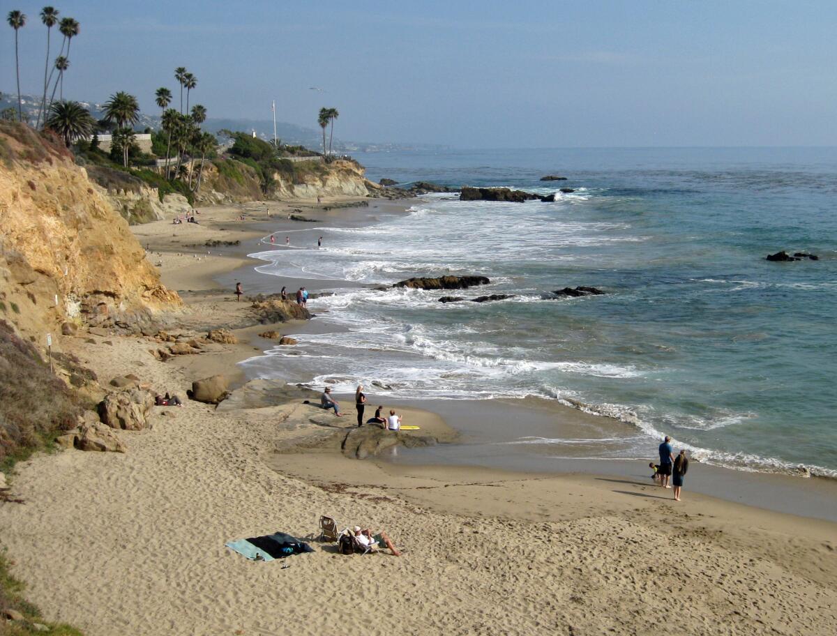 A view of people laying out on Laguna Beach with cliffs in the background.