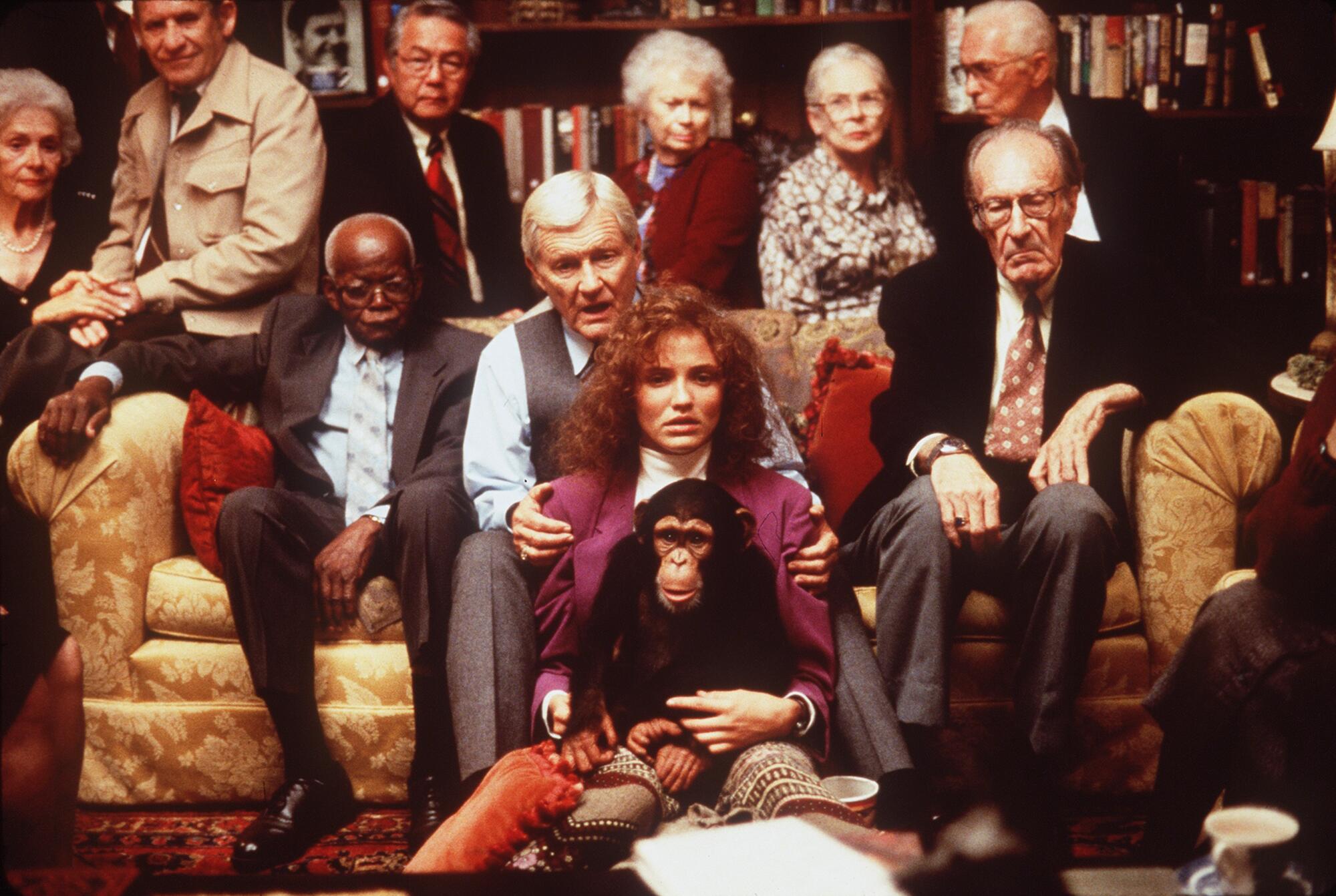 A diverse group of people sitting on two couches, with a woman in the center holding a chimpanzee