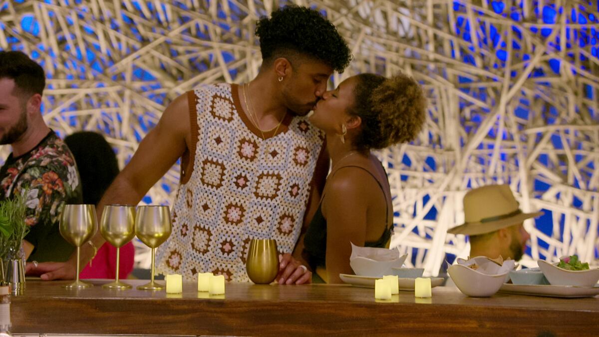 A man leans to kiss a woman as they stand at a bar.