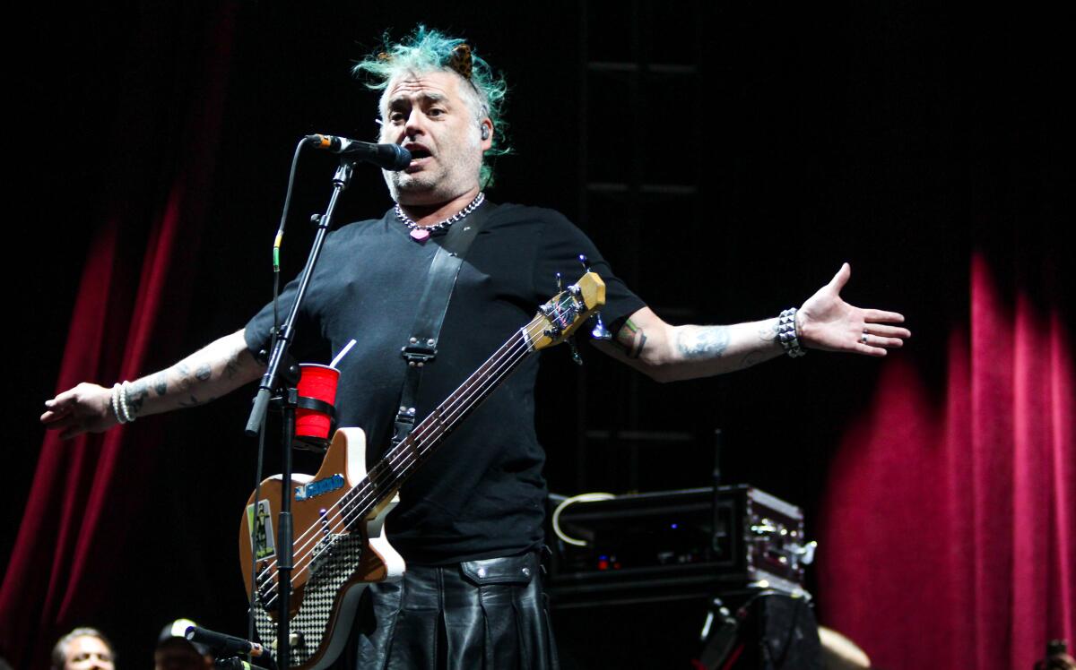 Fat Mike Burkett of NOFX onstage with a guitar, his arms spread wide