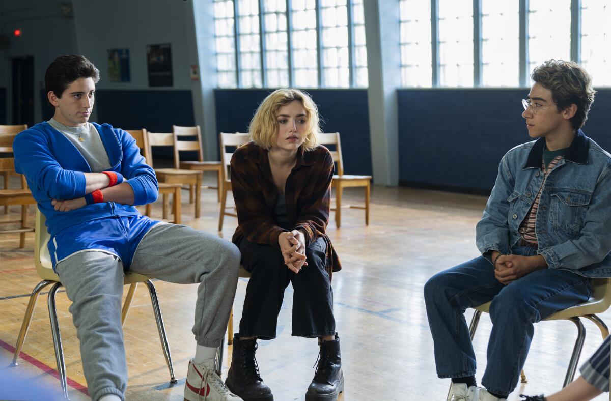 Three teens sitting on chairs in a high school gymnasium.