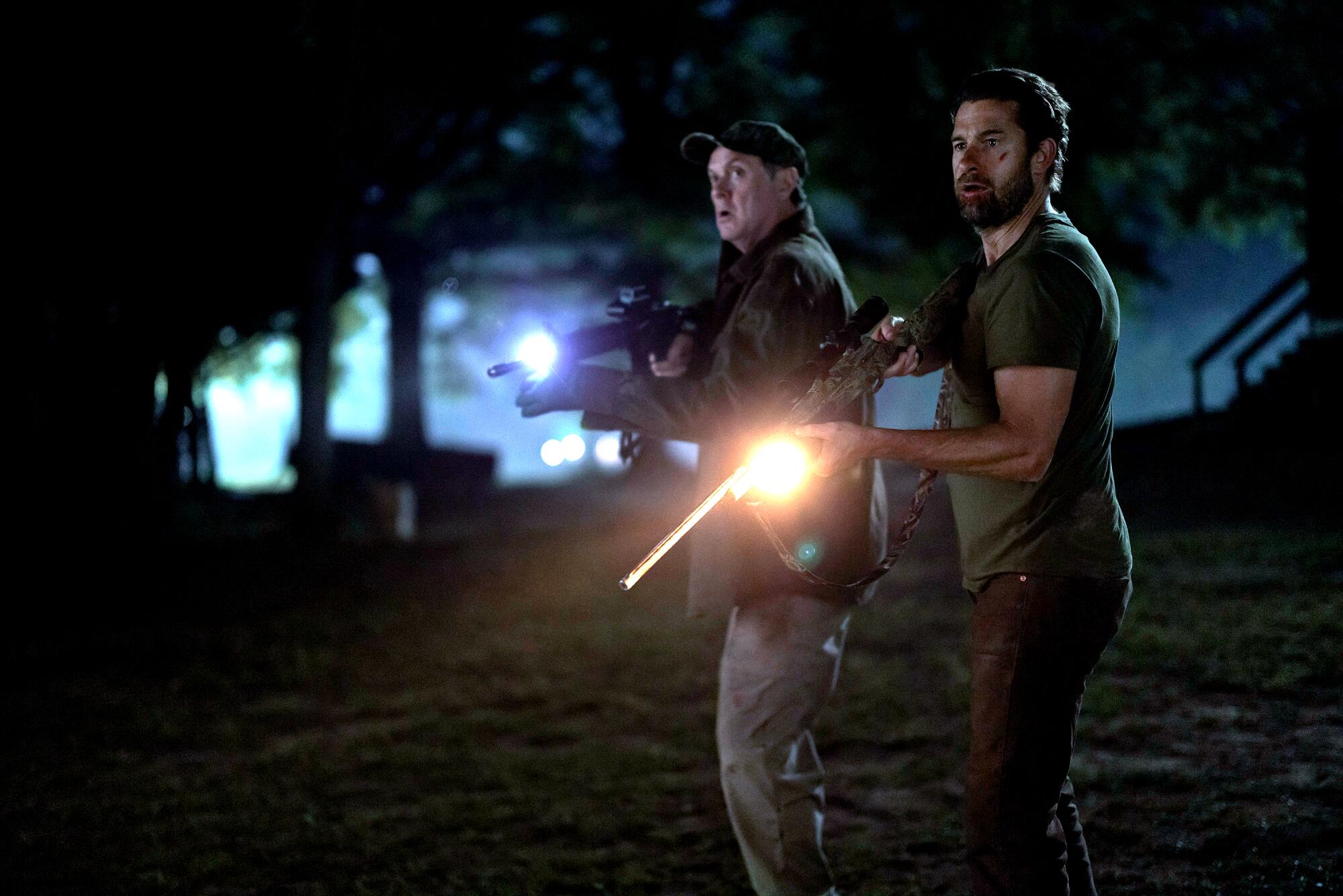 Two men hold rifles outdoors at night