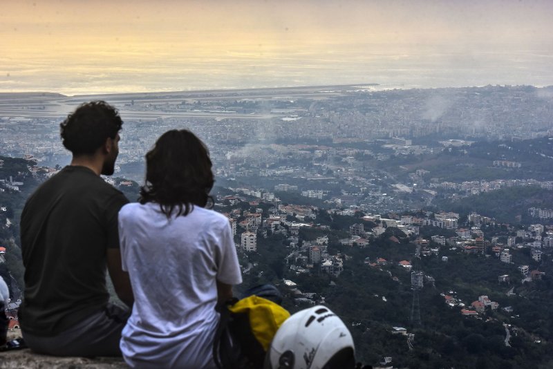 Lebanese people view the capitol city of Beirut from a high vantage point as smoke rises from between the buildings after Israeli airstrikes on Monday, October 7, 2024. The U.S. State Department on Monday said some 900 Americans, legal permanent residents and their family members have fled the country on U.S.-organized flights. Photo by Fadel Itani/ UPI