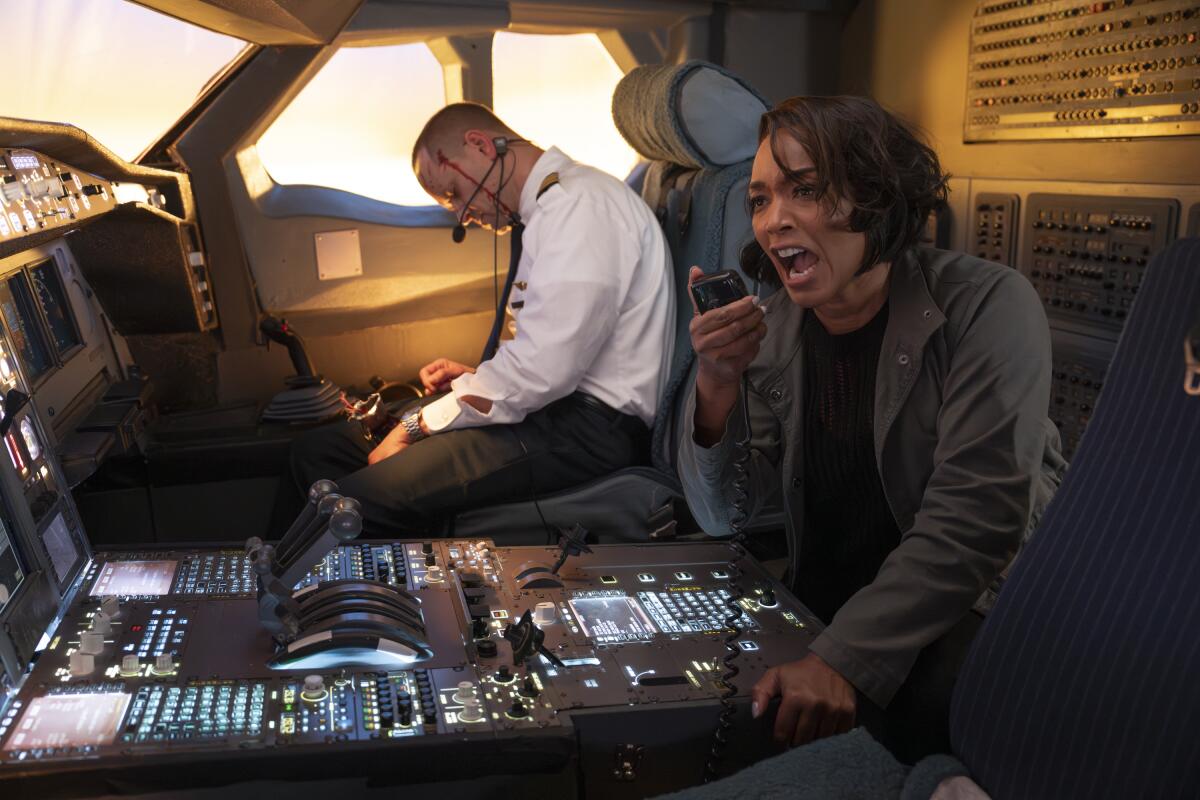 a woman talking into the radio in a cockpit while an injured man sits in a pilot's seat