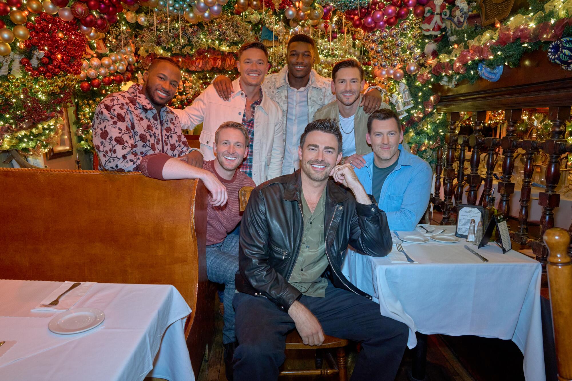 A group of seven men crowded together near a booth and table in a bar.