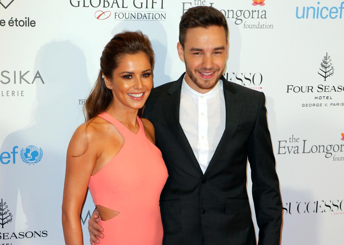 Liam Payne stands with his arm around the waist of Cheryl Cole on a red carpet