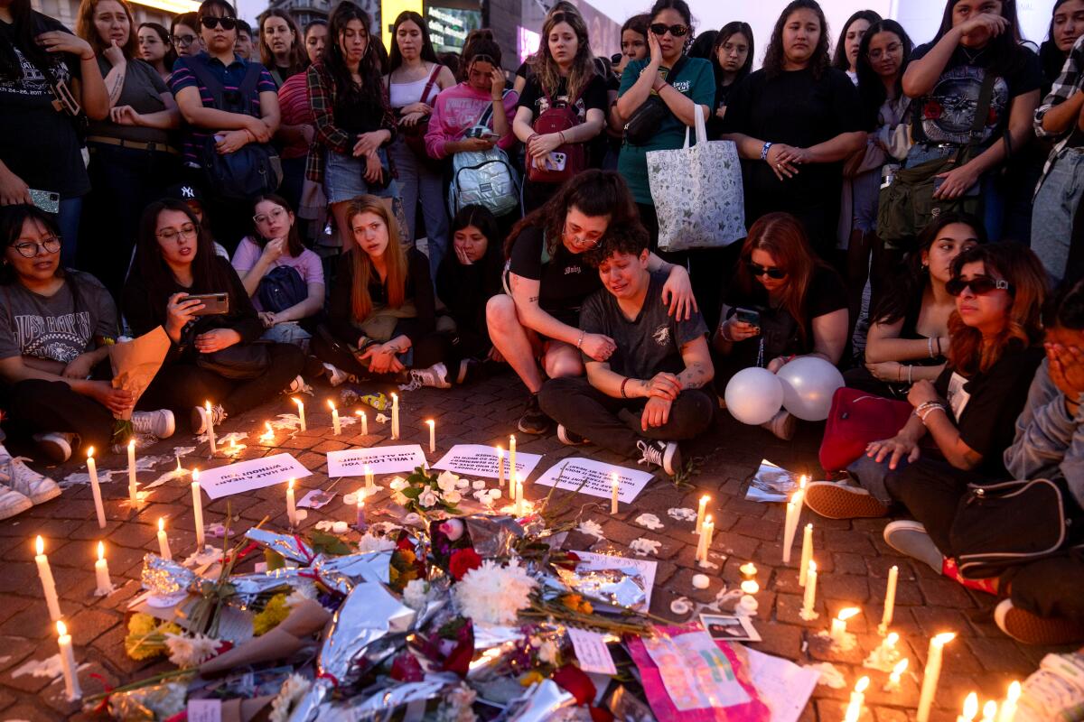 People in a semicircle around candles and a pile of flowers