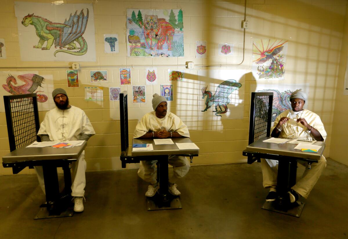 Three prisoners sit at desks