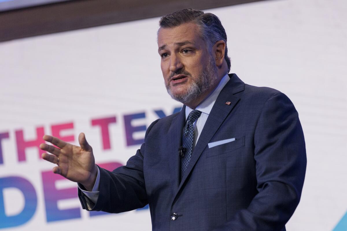 A man with a graying beard, in dark suit and tie, gestures with his hand while speaking