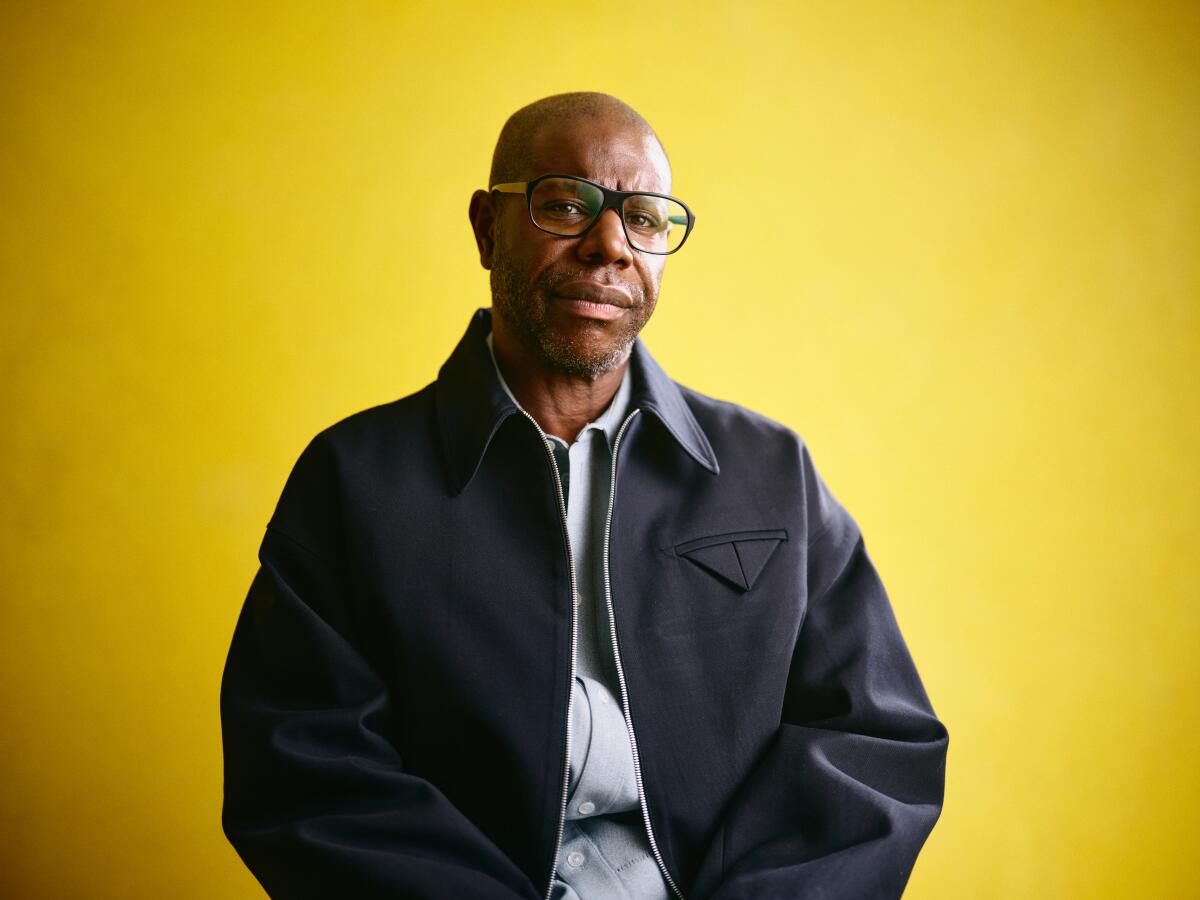 A man in eyeglasses poses in front of a yellow backdrop.