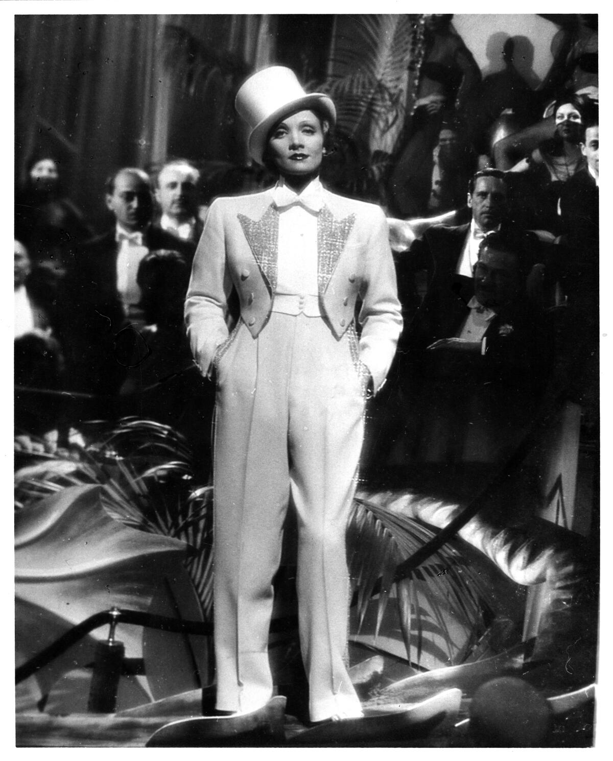 A woman stands in a white tuxedo and top hat.