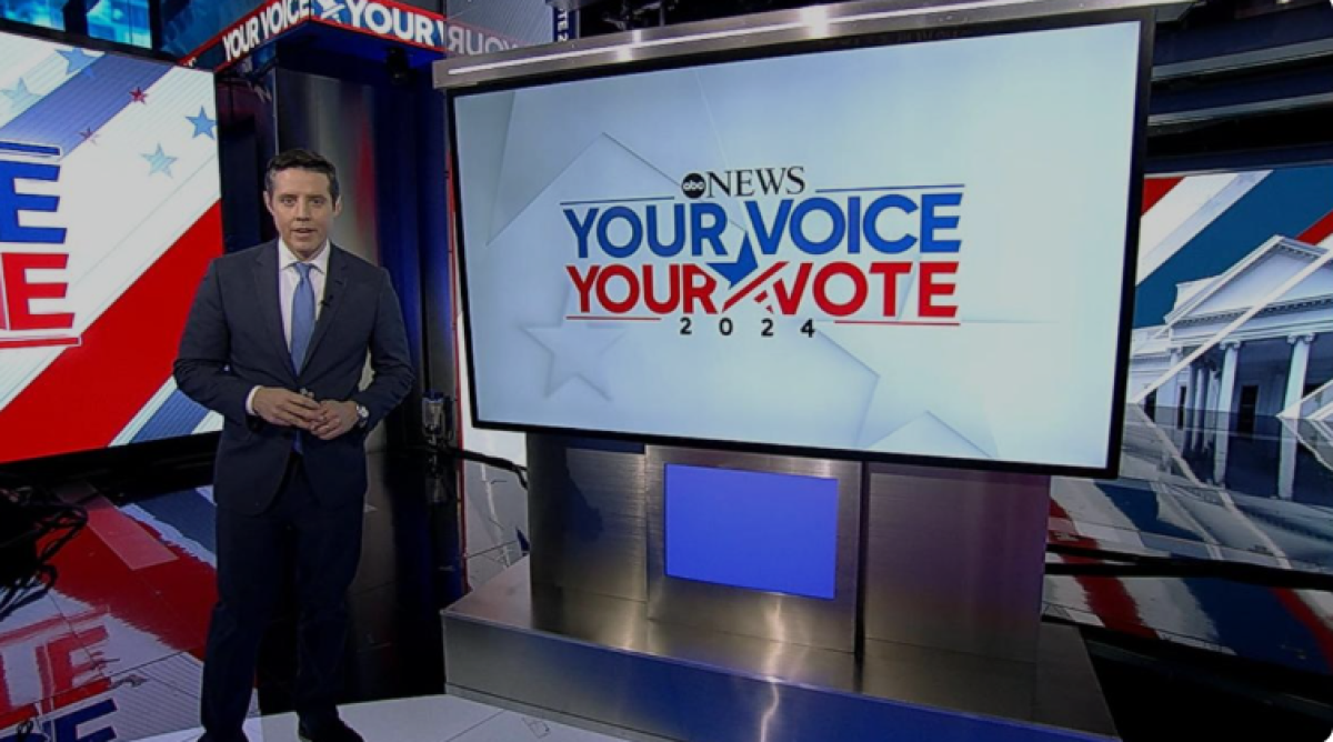 A man in a suit, who is a news executive for ABC News, stands in front of a screen that says "Your voice, your vote." 