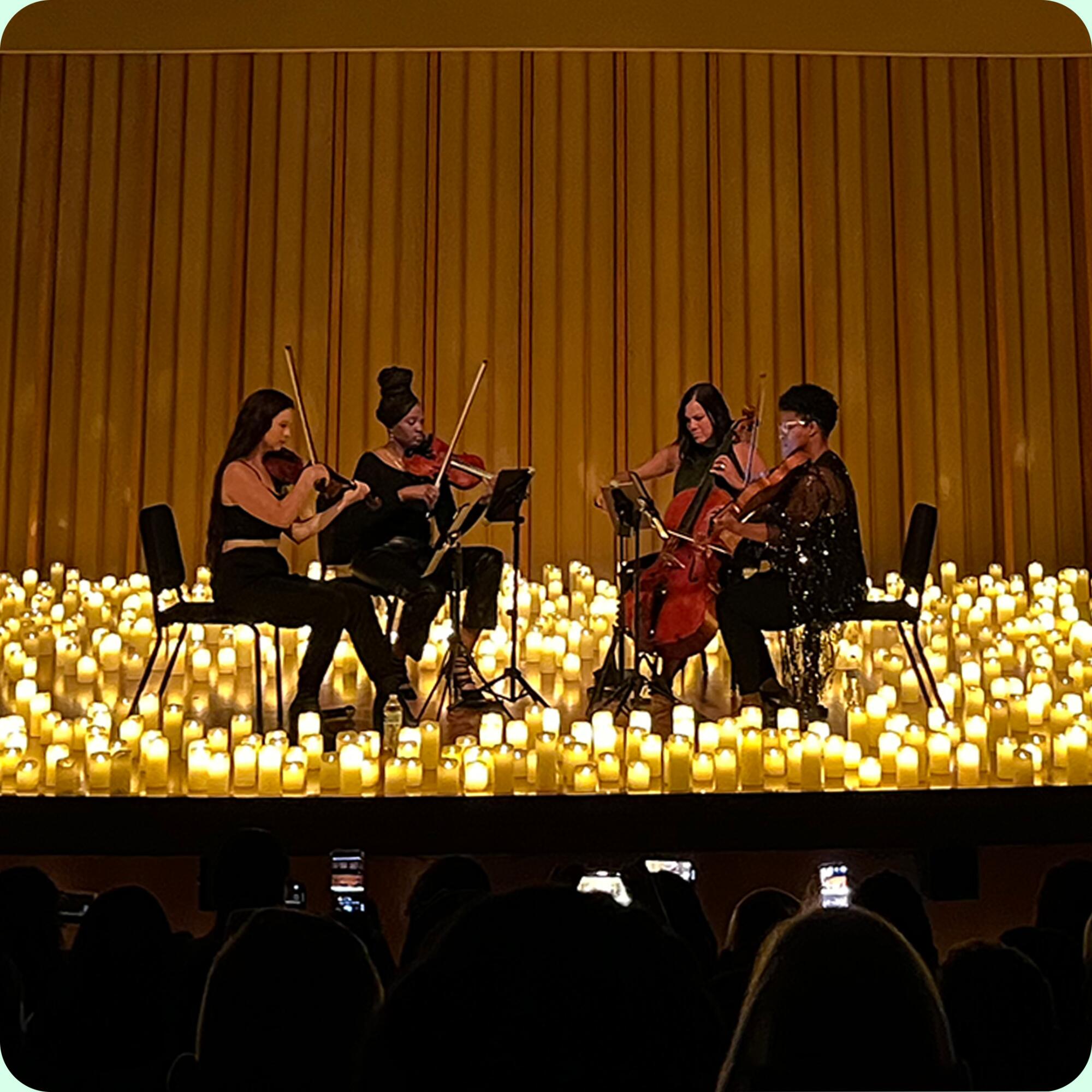 Four musicians play on a stage filled with candles.