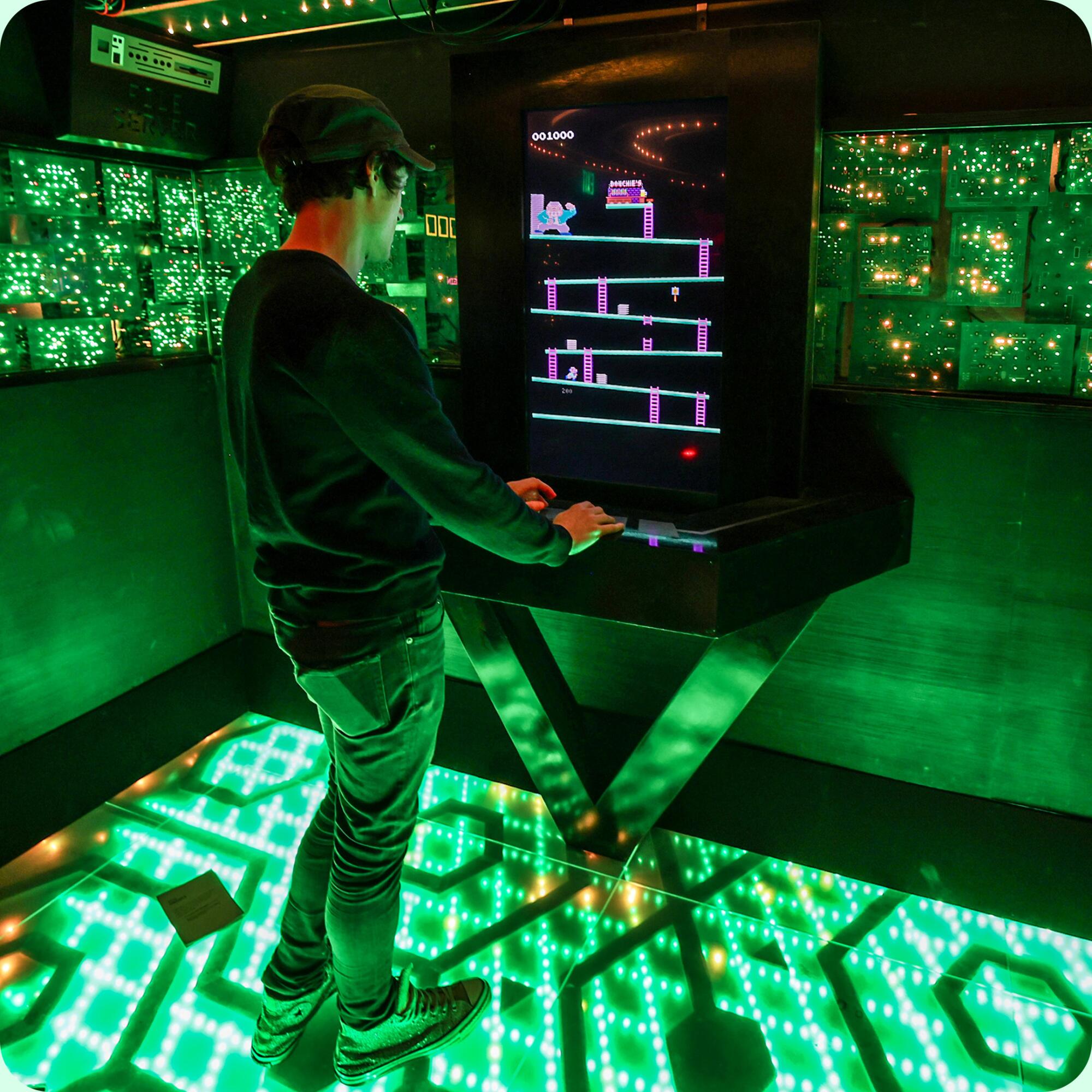 One person stands on a green-lighted floor playing the original Donkey Kong game on a modern arcade cabinet.