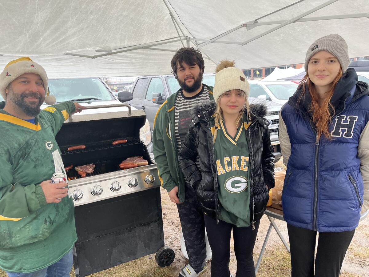 Four people standing beside a meat grill under a tent