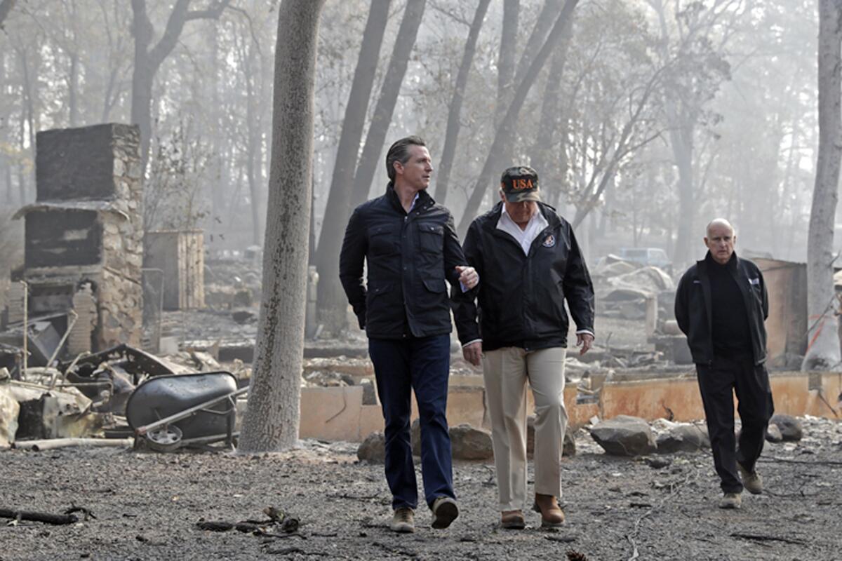 Three men walk among bare and blackened trees and the charred remains of burned homes