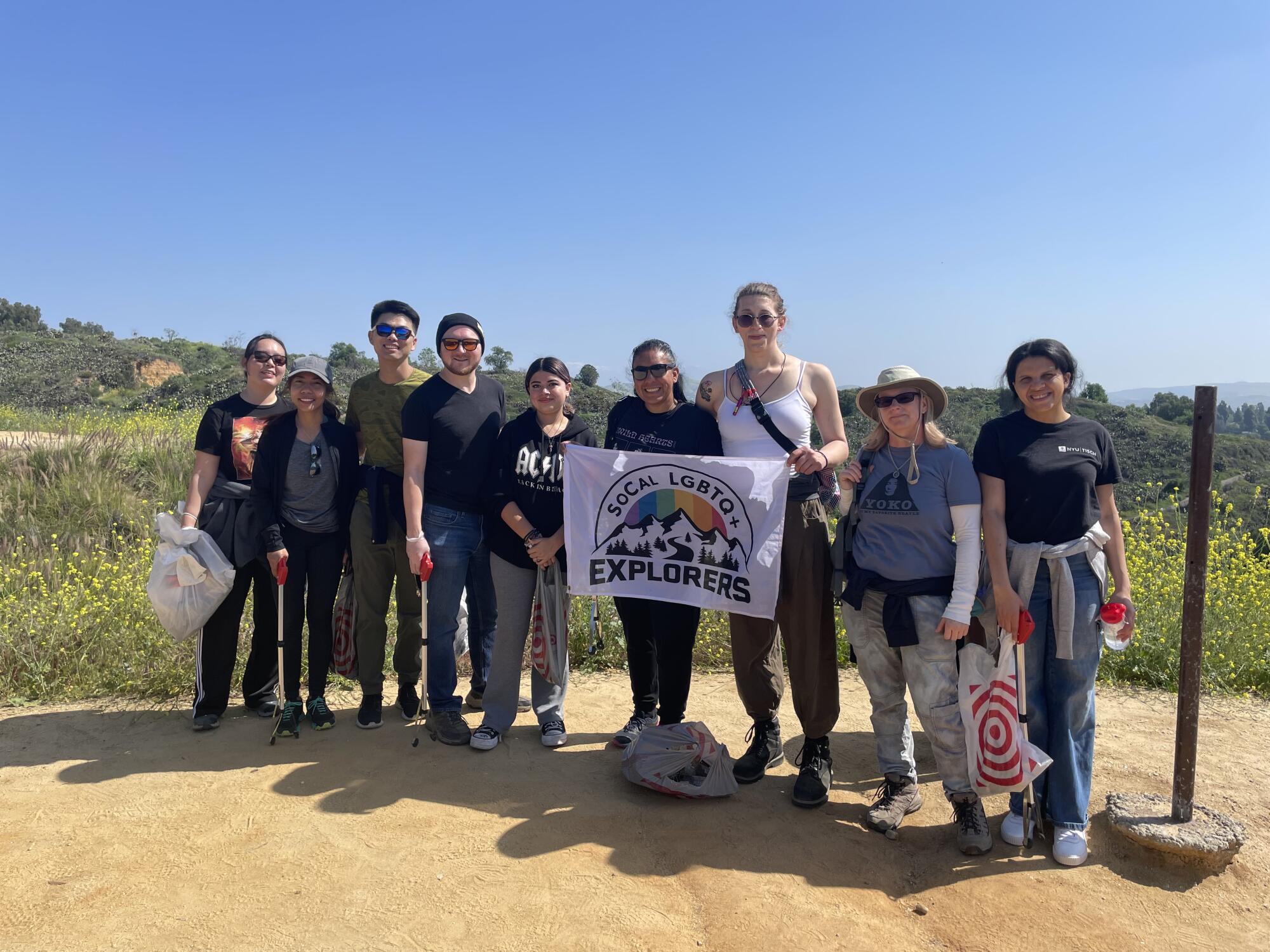 SoCal LGBTQ+ Explorers stand outdoors holding up a flag for their group