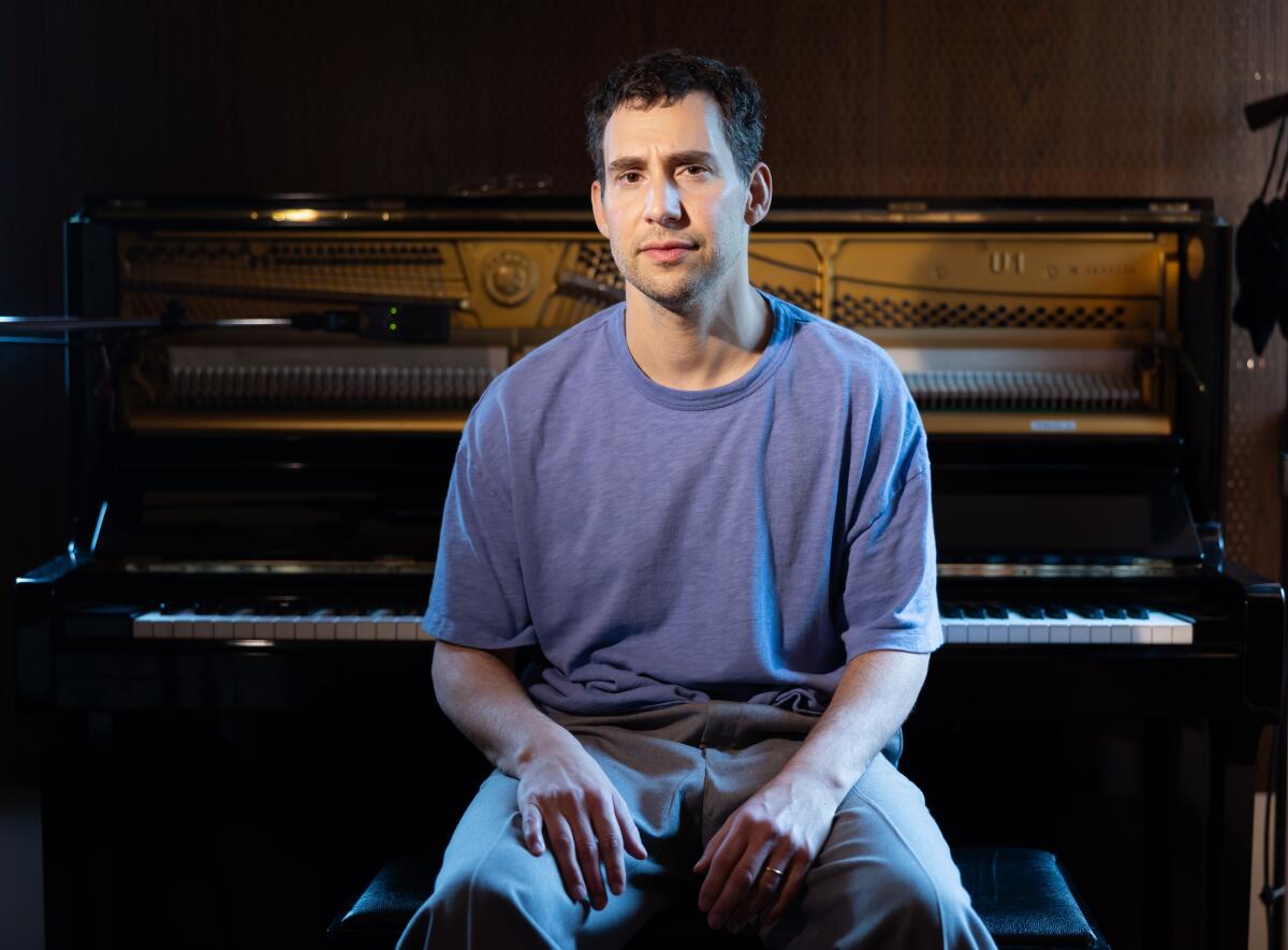 Man in a T-shirt sitting on a piano bench with the piano behind him