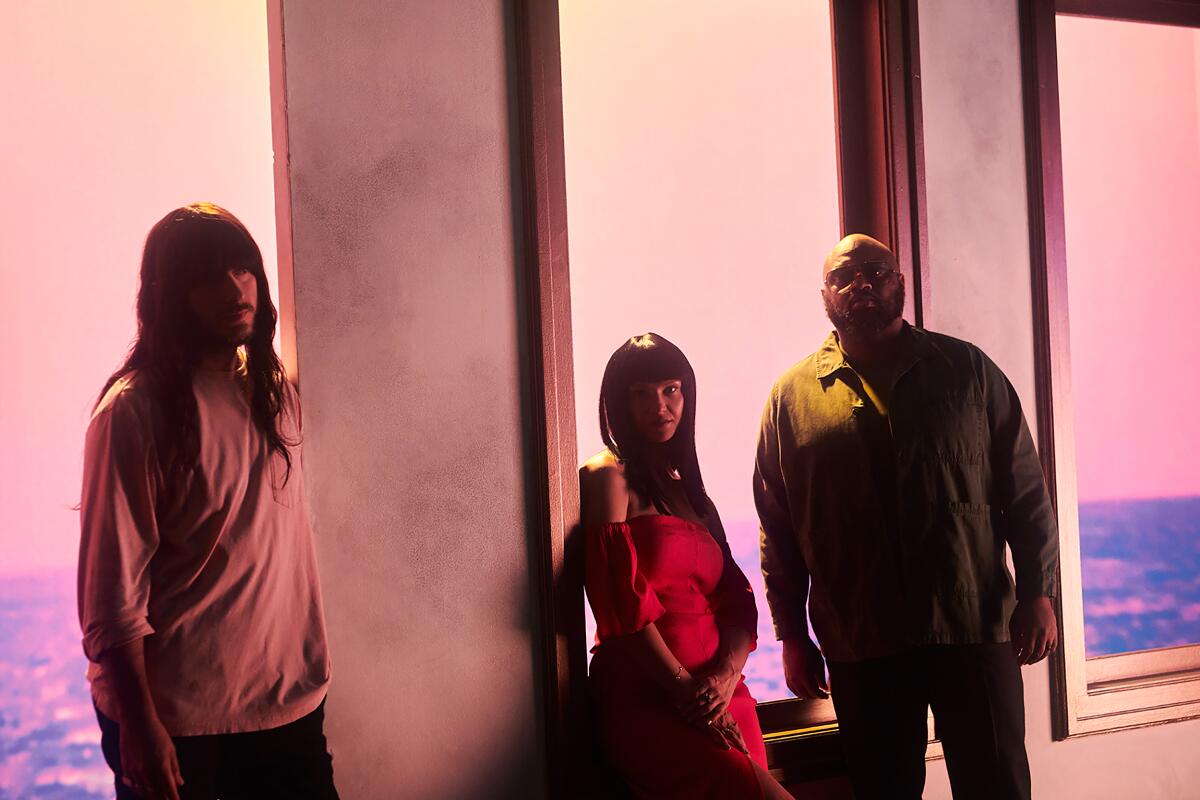 Three people stand in front of windows that overlook a body of water