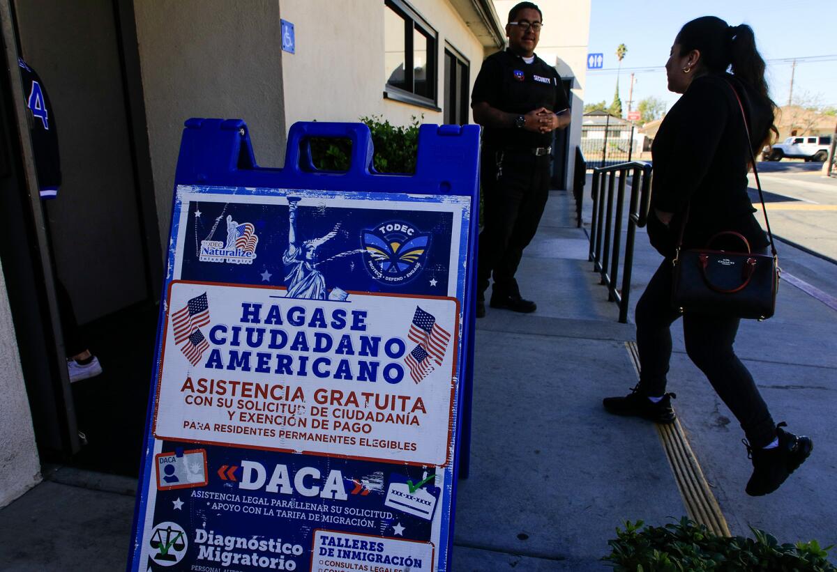 A security guard watches as a woman walks by a sign.