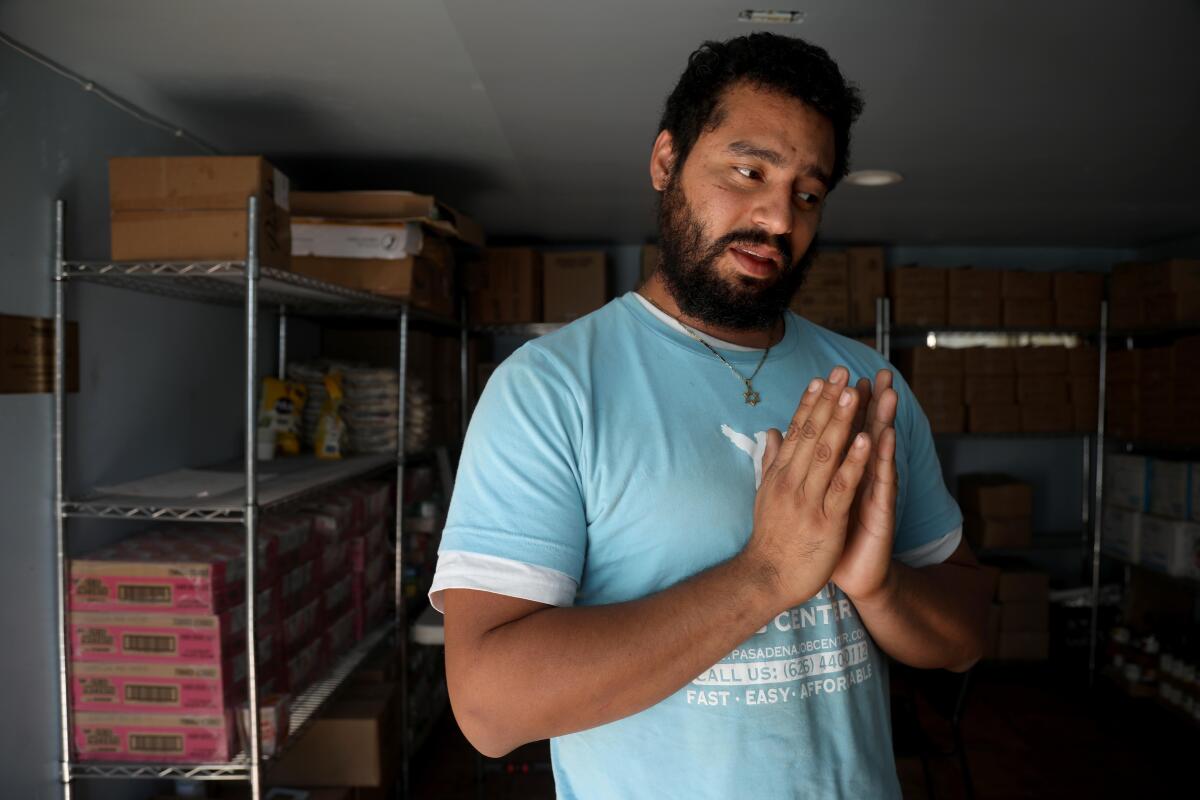 A man in front of shelves with cardboard boxes puts his hands together.