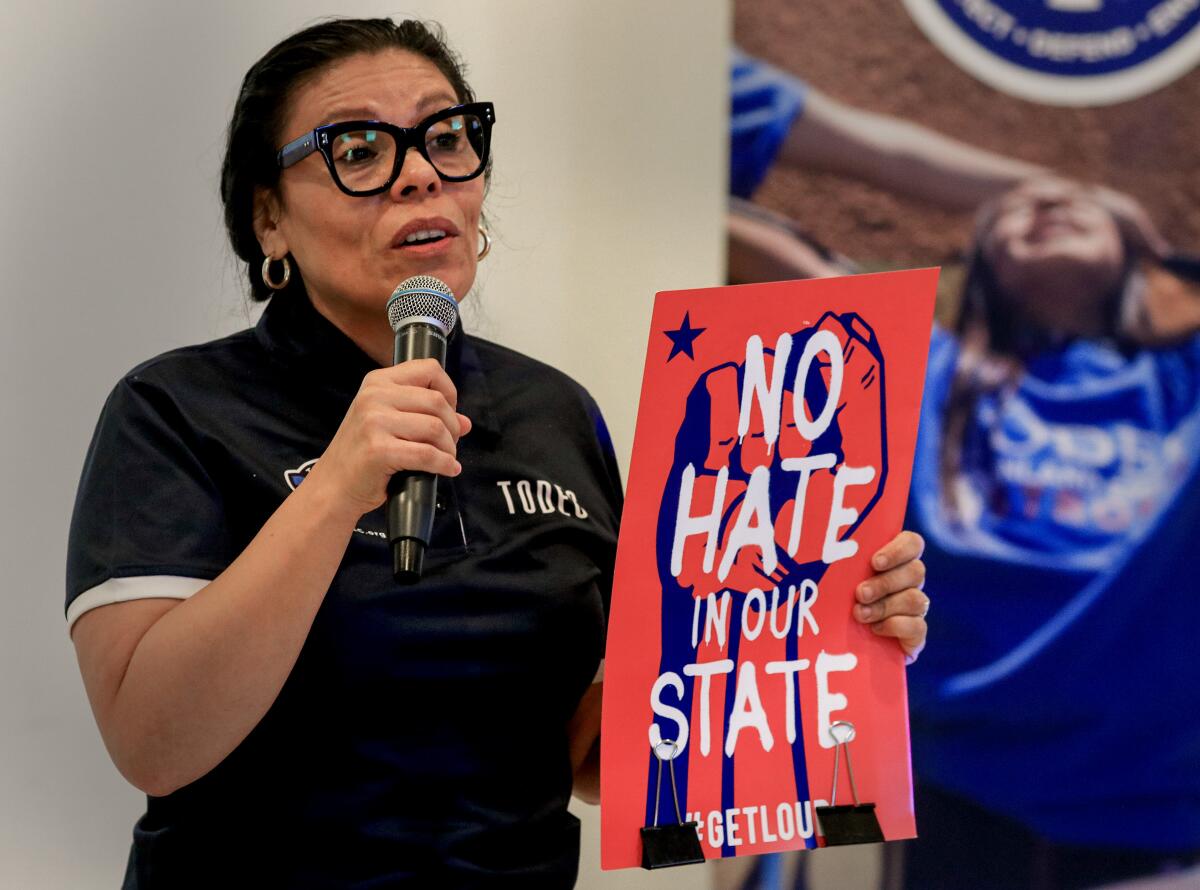 A woman holds a sign while talking on a microphone.