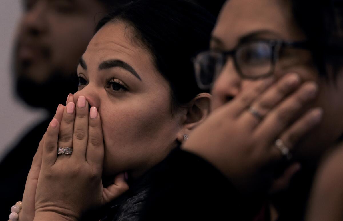 Two women cup their faces with their hands.