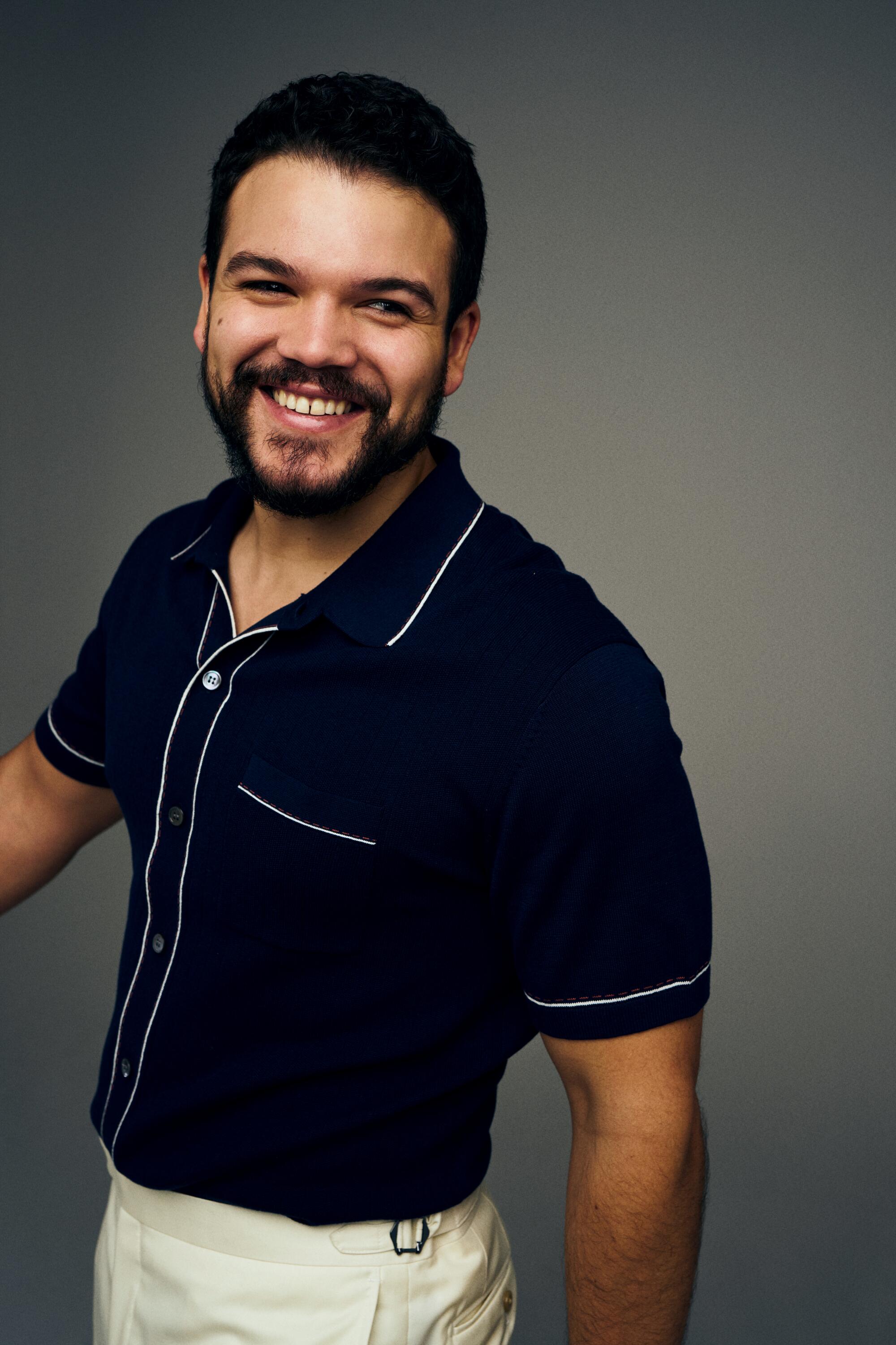 Josh Rivera with dark hair and a beard in a blue shirt and white pants.