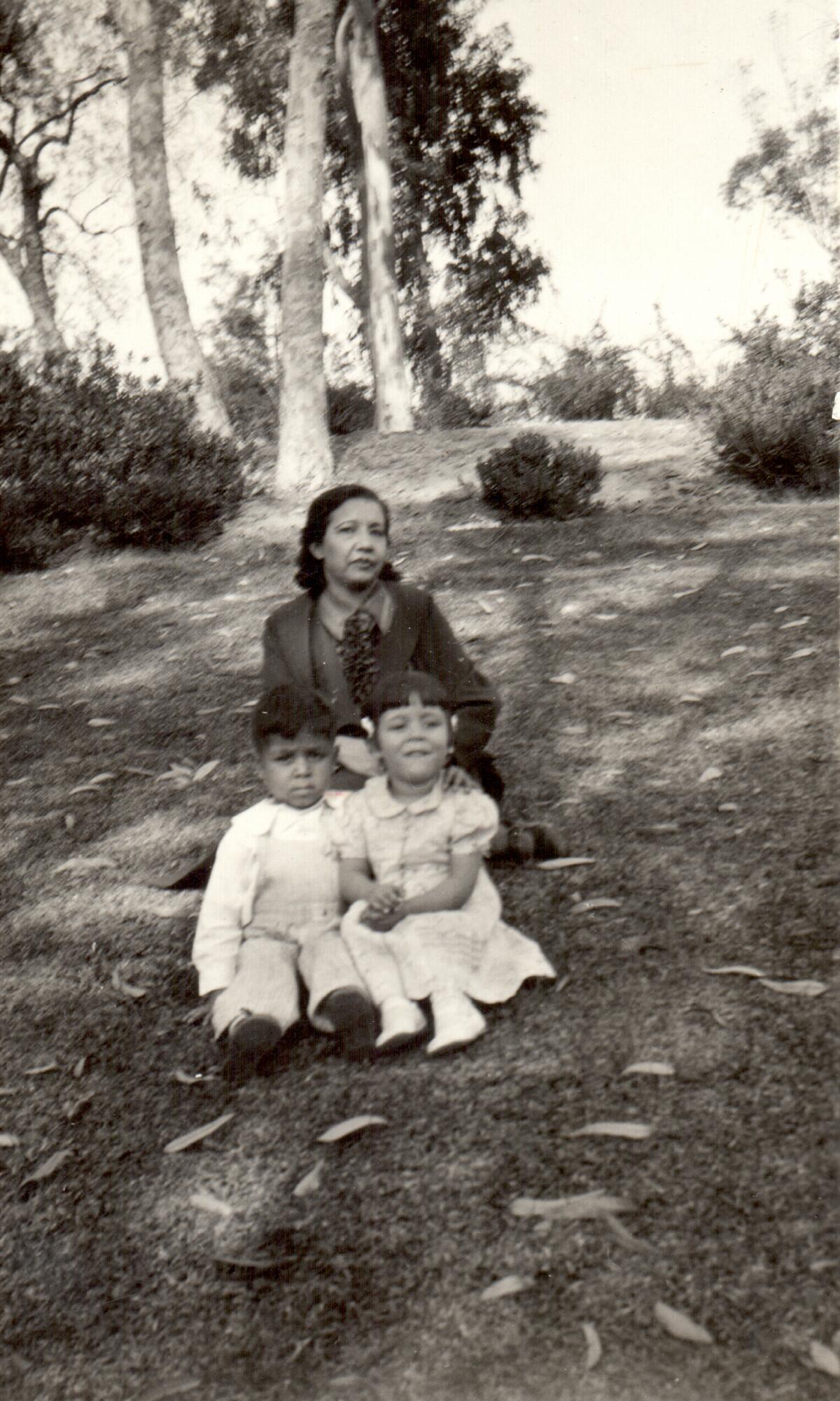 A black and white photo of a Latina woman sitting outside with two Latino children