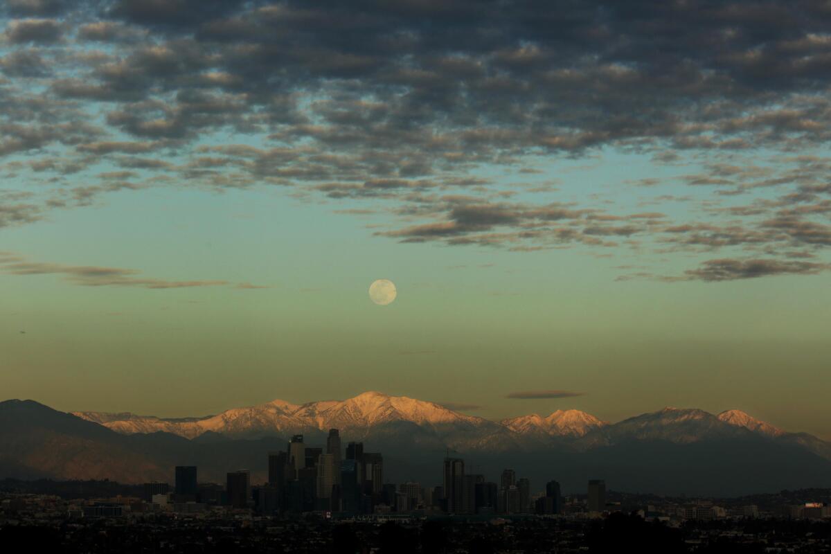 The moon rises above the snowcapped San Gabriel Mountains and the Los Angeles skyline