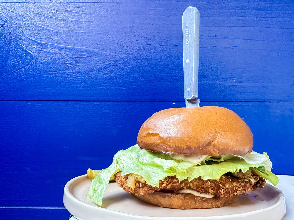 A chicken schnitzel sandwich on a plate with a knife standing up in its center